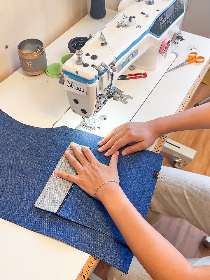 Mains guidant du denim sous une machine à coudre dans l’atelier Nabou